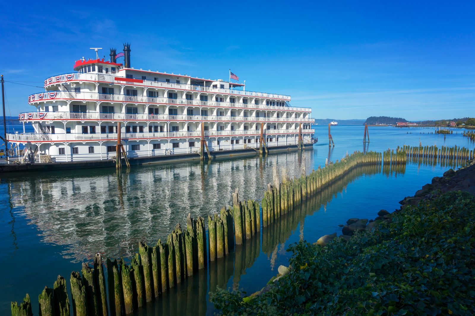 A large white riverboat docked beside old wooden pilings on the Columbia River at Astoria