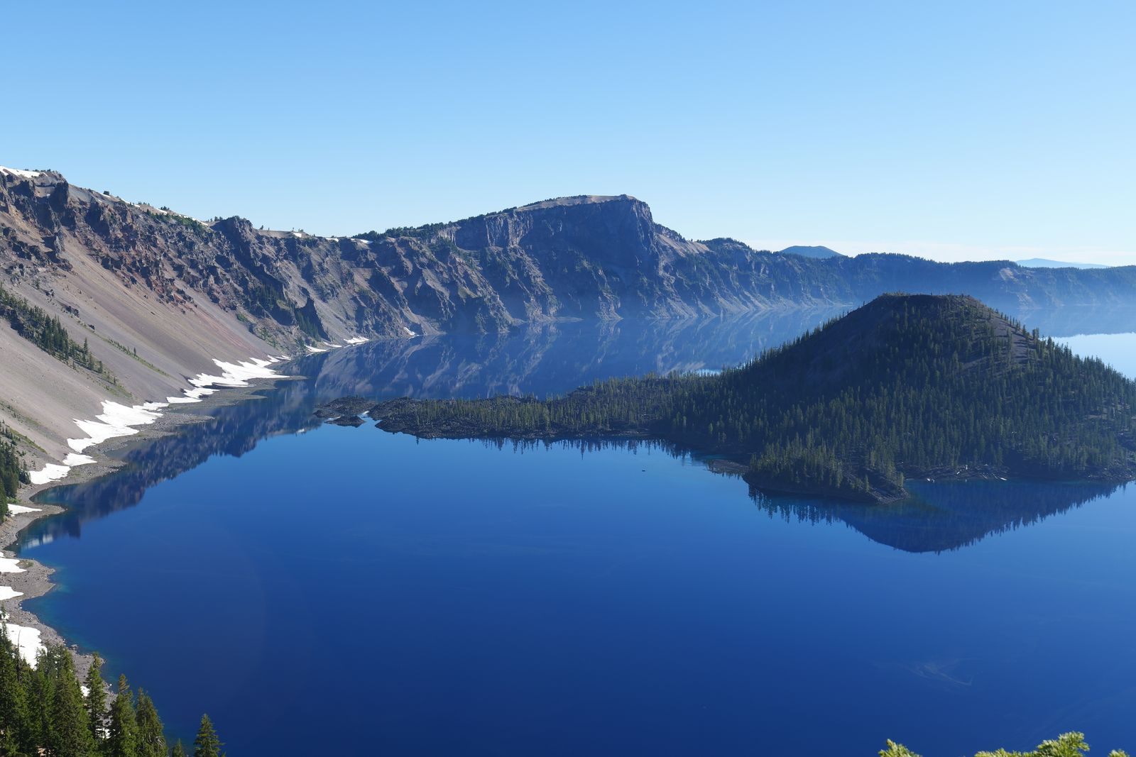 Wizard Island reflected in still Crater Lake below the snow-streaked caldera rim